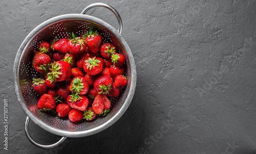 Fresh juicy red strawberries in stainless steel colander on Dark grey black slate background 