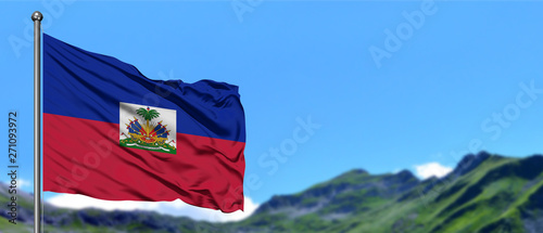 Haiti flag waving in the blue sky with green fields at mountain peak background. Nature theme.