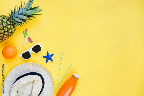 Summer vacation background. Straw hat, white sunglasses, tropical fruits, fresh juice and cocktail accessories over yellow background. Copy space, flat lay.