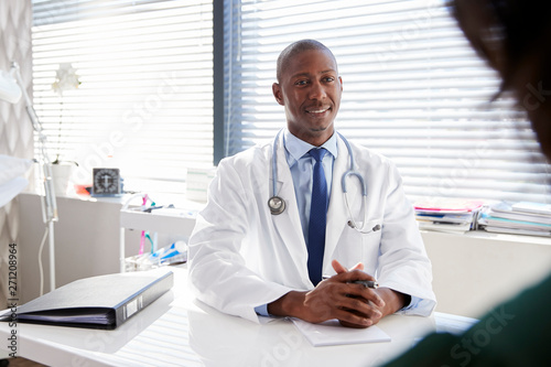 Female Patient In Consultation With Doctor Sitting At Desk In Office