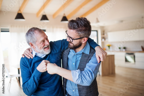 An adult son and senior father indoors at home, making fist bump.