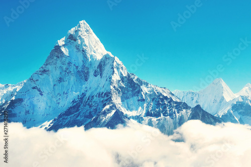Snow capped rugged mountain peak towers of Ama Dablam above the cloud tops.