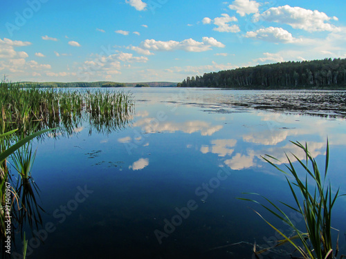 Summer idyllic landscape with lake and sky. Bright day view with blue sky and white clouds and reflection in calm water surface. Lake Chebarkul, South Ural, Russia.