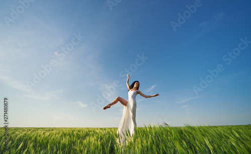 Yoga and fit. Flying dancer in the air. Happy woman ballerina in white fabric skirt posing on Green field. Summer or concept