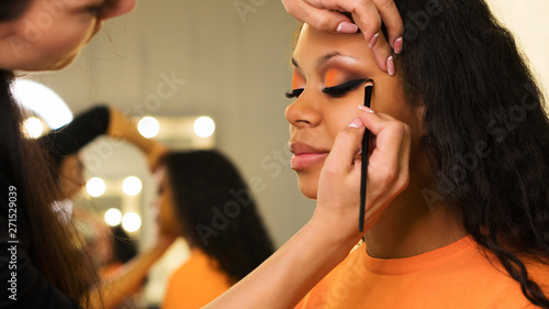 Makeup artist draws arrows on eyelids of african girl. Evening make-up. Closeup portrait side view