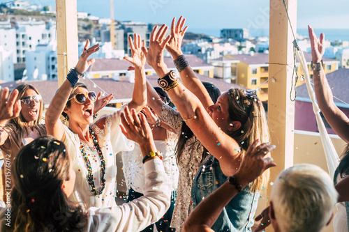 Group of happy young people caucasian women with terndy fashion clothes celebrate together with a lot of fun with coloured confetti and nice scenic view on the city from rooftop- happiness and joyful