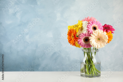 Bouquet of beautiful bright gerbera flowers in glass vase on table against color background. Space for text