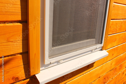 Mosquito net on a plastic window in a wooden house. Close-up. Background.