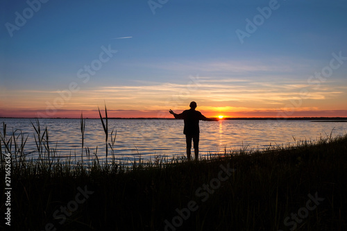  The man 58 years old on the shore of Svityas Like admires the sunset in the summer in Ukraine. The sun is on the man's palm. Self-isolation concept. The symbiosis of man and nature.