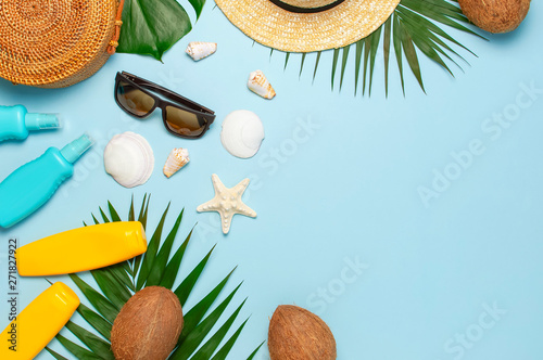 Summer composition flat lay. Round trendy rattan bag straw hat sunglasses tropical palm leaves coconut sunscreen seashells on blue background. Top view copy space. Creative fashion vacation backdrop