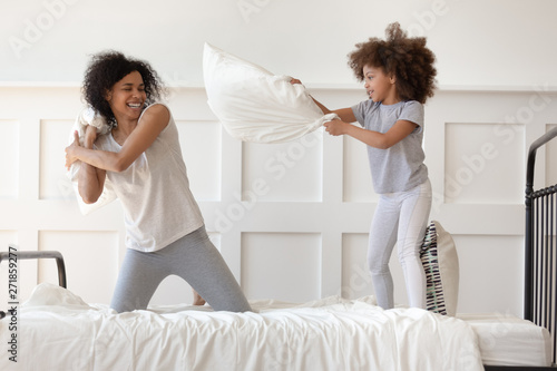 Happy african mom and daughter having pillow fight on bed