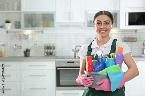 Portrait of young woman with basin of detergents in kitchen. Cleaning service