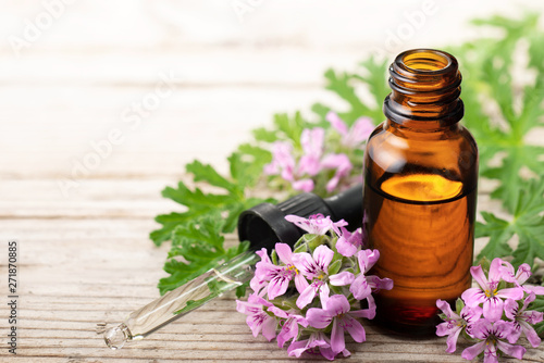 Geranium essential oil with fresh geranium flowers, on the old wooden board