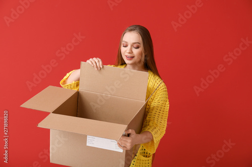 Young woman with open cardboard box on color background
