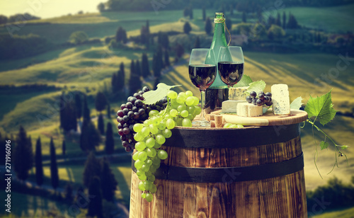 Red wine bottle and wine glass on wodden barrel. Beautiful Tuscany background.