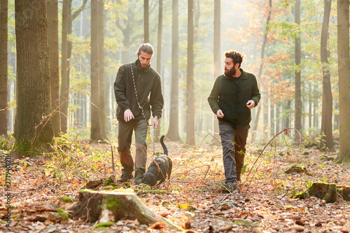 Zwei Jäger mit einer Bracke als Jagdhund im Wald