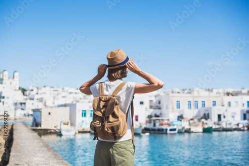 Traveler girl enjoying vacations in Greece. Young woman wearing hat looking at greek village with sea. Summer holidays, vacations, travel, tourism concept.