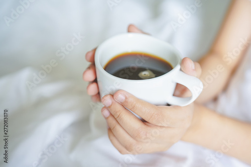 girl's hand hold cup of hot coffee on white bed