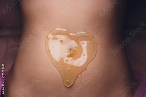 specialist cosmetologist professional removes unwanted hairs from female client's body.shugaring of legs and bikini area in the spa salon honey and sugar. heart shape