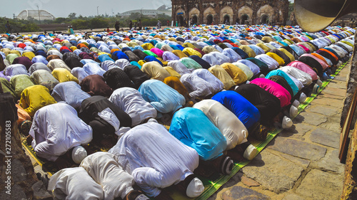 A gathering of Muslim men and children bowing down and offering Namaz prayers on the occasion of Eid'Al-Fitr 2019. They are dressed in kurta pyjamas of many colours, and wearing traditional skullcaps