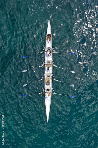 Aerial drone bird's eye view of sport canoe operated by team of young women in emerald open ocean sea
