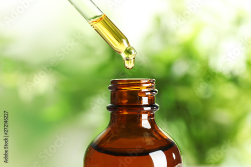 Dripping natural tea tree essential oil into bottle on blurred background, closeup