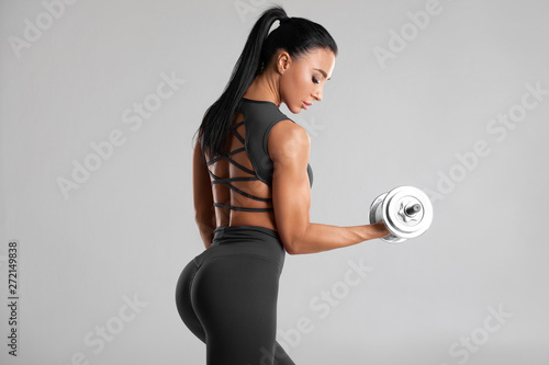 Fitness woman doing exercise for biceps on gray background. Muscular woman workout with dumbbells