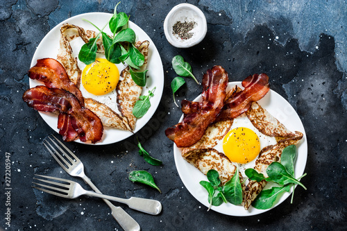 Stuffed egg crepes with bacon and arugula - delicious nutritious brunch on a dark background, top view. Flat lay
