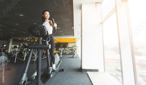 Fitness workout. Girl exercising on elliptical trainer in gym