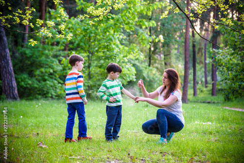 Young woman mother applying insect repellent to her two son before forest hike beautiful summer day or evening. Protecting children from biting insects at summer. Active leisure with kids