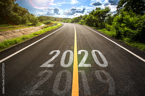 The word 2020 written on highway road in the middle of empty asphalt road at golden sunset and beautiful blue sky. Concept for new year 2020. 