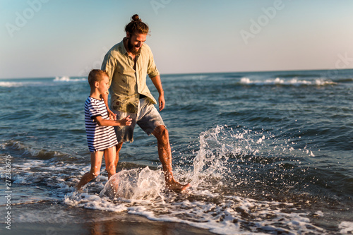 Happy father and son, man & boy child, running and having fun in the sand and waves of a sunny beach