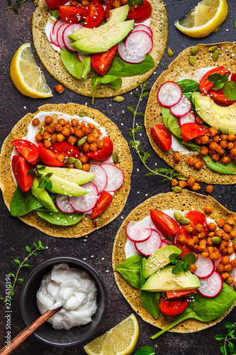 Vegan tacos with baked chickpeas, avocado, sauce and vegetables on dark background, top view.