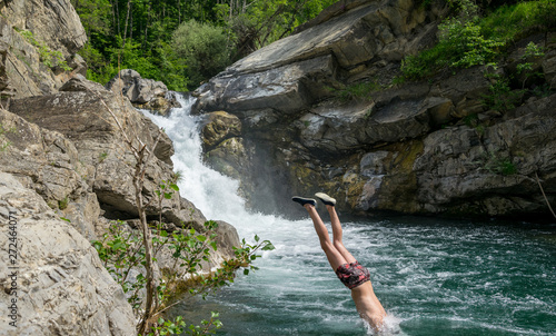 Young man diving in a natural pool in front a waterfall