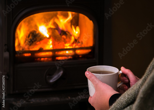 Woman having a hot cup of rink at the fireplace. Burning firepla