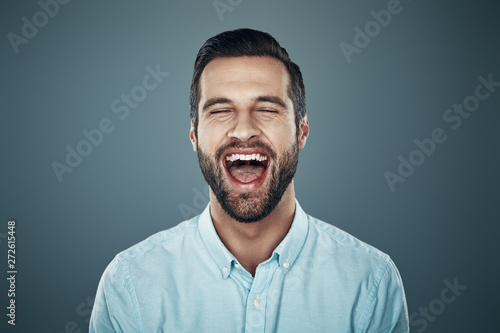 So much fun! Handsome young man laughing while standing against grey background
