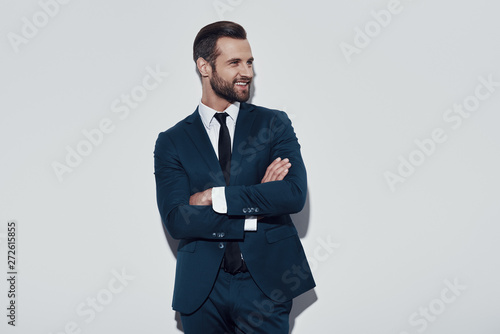 Handsome businessman. Charming young man keeping arms crossed and smiling while standing against grey background