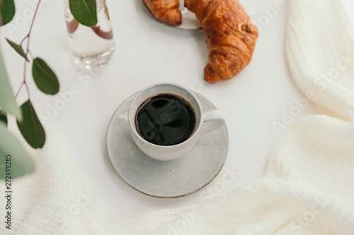 Cup of black coffee with croissant on white table. The concept of breakfast.