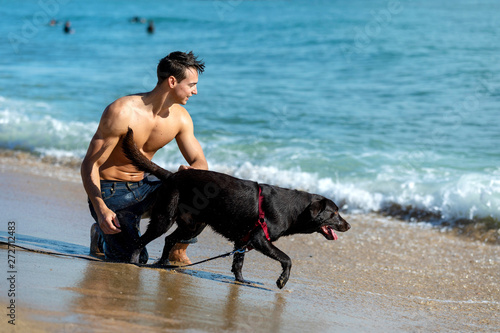 young caucasian male playing with dog on beach during sunrise or sunset.