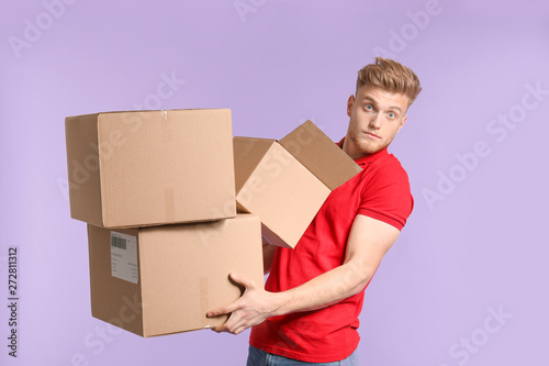 Young man with cardboard boxes on color background