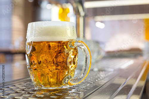 Freshly poured draft lager beer in a dimpled glass mug on stainless steel counter in a modern pub. Space for text.