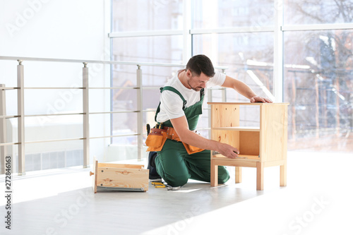 Handyman in uniform assembling furniture indoors. Professional construction tools
