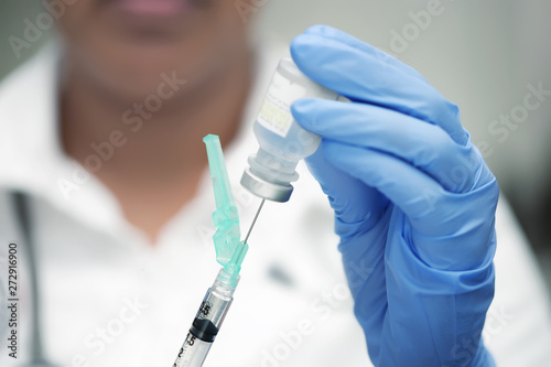 Medical professional with white scrubs and blue nitrile gloves, preparing a vaccine shot.