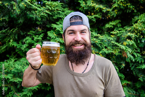 Beer is great summer drink. Bearded man holding beer mug on summer nature. Brutal hipster drinking refreshing beer on summer day. Happy drinker enjoying summer time