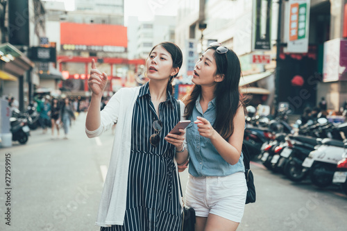 Friends having fun outdoors gathered together looking at smart phone on holiday. two young asian girls traveler holding cellphone pointing searching direction on street with scooter taiwan taipei