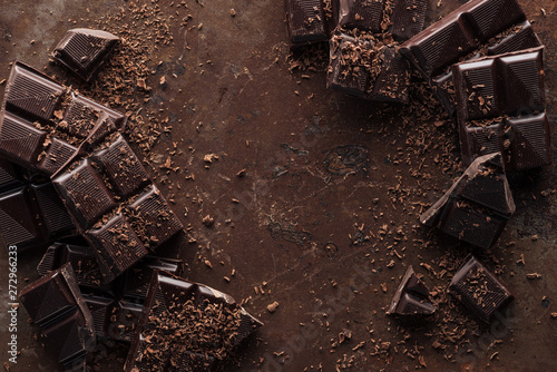 Top view of pieces of chocolate bar with chocolate chips on rust metal background