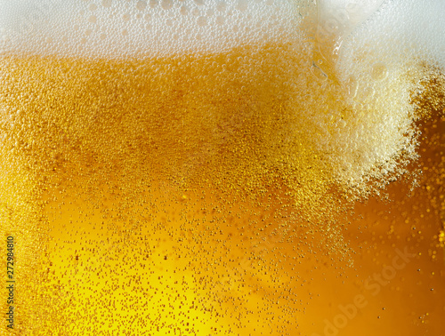 Close up view of floating bubbles in light golden colored beer background. Texture of cooling summer's filtered drink with foam and macro fizz on the glass wall. Fizzing or floating up to top of