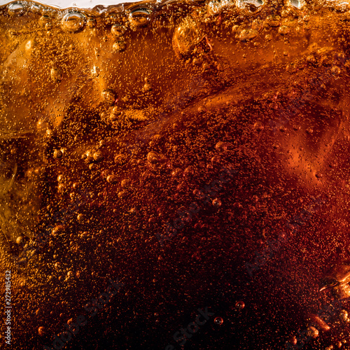 Close up view of the ice cubes in dark cola background. Texture of cooling sweet summer's drink with foam and macro bubbles on the glass wall. Fizzing or floating up to top of surface.