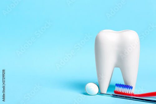 Oral dental hygiene. Dental mirror with toothbrush near healthy white tooth model on light blue background. Free space for your text.