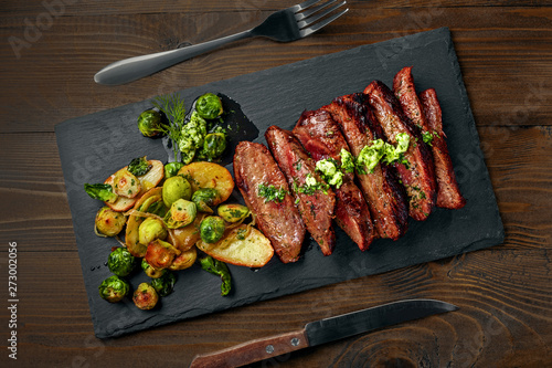 Medium rare meat hanger steak with brussels sprouts, potatoes and onion with herb sauce on a table.. Delicious healthy food. Top view above.